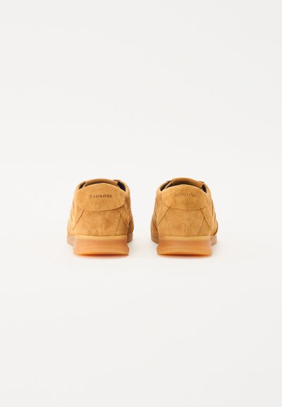 Zapatillas de ante en color marrón claro con un acabado texturizado, forma curva y suelas de goma. Nombres de las marcas "Proenza" y "Schouler" grabados en el talón.