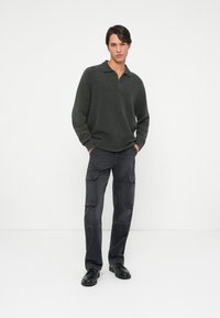 Pullover a maglia verde scuro con colletto, abbinato a pantaloni cargo grigio scuro. Tessuto liscio, vestibilità rilassata e diversi taschini sui pantaloni.