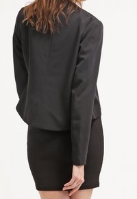 Svart kavaj med en slät struktur och skräddarsydd passform, kombinerad med en matchande svart kjol för ett enhetligt utseende.
