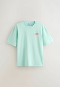 Lyse turkisd kortærmet T-shirt med rund hals, med lille pink og hvid "DAILY GRIND" tekst på øverste venstre bryst.