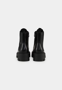 Bottines en cuir noir avec semelles compensées épaisses, languettes à l'arrière et fermetures éclair latérales, vues de dos sur fond blanc.