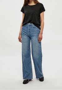 Černé tričko s krátkým rukávem v kombinaci s vysokými, širokými světle modrými džínami se třepícími lemy a opotřebovaným vzhledem.