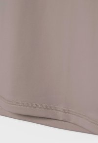 Primo piano di orlo in tessuto beige con cucitura doppia su materiale tessile liscio.