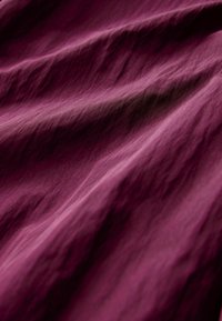 Teksturoitu kangas syvässä burgundin värissä, jossa on pehmeitä aaltoja ja poimuja, korostaen sileää, mattapintaista viimeistelyä ja rikasta sävyä.