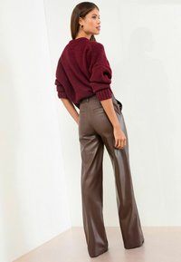 Burgundski pleteni pulover s okruglim izrezom i okrenutim rukavima, uparen s smešnim širokim hlačama od umjetne kože koje imaju stražnje džepove.