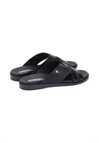 Sandalias de cuero negro con suela plana, con un diseño de tiras cruzadas y un pequeño detalle dorado. Textura suave y estilo minimalista.