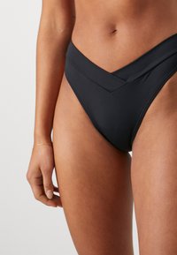 Svart bikini-bunn med V-formet midje, glatt tekstur og minimalistisk design, med ensfarget farge og uten synlige mønstre.