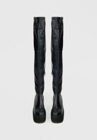 Čierne čižmy nad kolená z umelej kože s hladkou textúrou, vybavené robustnou podrážkou a bočnými zipsami pre jednoduché obúvanie.