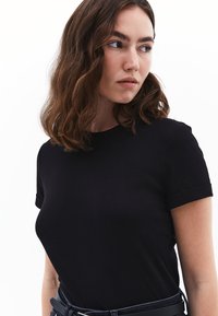 Černé tričko s krátkým rukávem vyrobené z bavlny, s kulatým výstřihem a ohrnutými manžetami. Hladká textilie s upnutým siluetou.