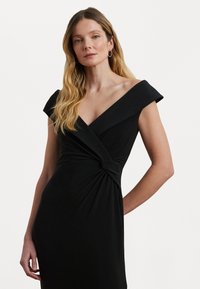 Svart figurnära klänning med axelbandsfria kap sleeves, omslag design och en knuten detalj vid midjan, tillverkad av mjukt, stretchigt tyg.