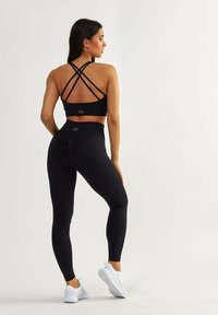 Czarny stanik sportowy z krzyżującymi się paskami na plecach, w zestawie z wysokimi czarnymi legginsami. Gładki materiał o gładkiej fakturze i minimalnym brandingu.