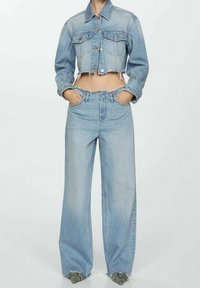 Chaqueta corta de mezclilla azul claro con dos bolsillos delanteros, combinada con vaqueros de tiro alto y pierna ancha. Detalles desgastados en el dobladillo de ambas prendas.