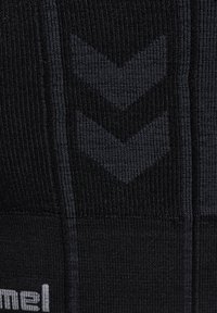 Zwarte compressietights met een geribbelde textuur, subtiel chevronpatroon en een logo aan de zoom, ontworpen voor sportief gebruik.