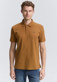 Brun polo shirt i en blød bomuldsblanding med en krave, tre-knaps placket og et lille logo på venstre bryst.