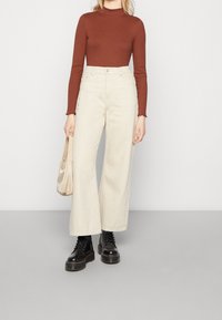 Hellbeige weite Hose mit hoher Taille, kombiniert mit einem eng anliegenden rostfarbenen Langarmoberteil und schwarzen Schnürstiefeln.