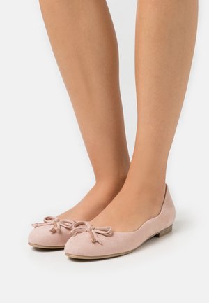 Lys rosa ruskindsballetsko med rund tå, der har en dekorativ sløjfedetalje på hver sko og en lav, flad sål.