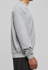 Sudadera gris de tejido suave y texturizado con cuello redondo, hombros caídos y puños y dobladillo acanalados, mostrada de lado.