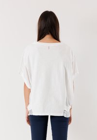 T-shirt bianco, comodo e leggero, con maniche corte e scollo a giro. Fessure laterali e un piccolo dettaglio con etichetta sul retro.