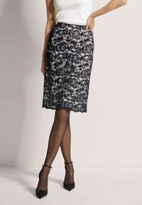 Schwarze Spitzen-Bleistiftrock mit Blumenmustern, knielang, mit texturiertem Finish und gewelltem Saum. Kombiniert mit schwarzen Absätzen und transparenten Strümpfen.