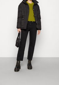 Schwarze gepolsterte Jacke über einem grünen gerippten Pullover, kombiniert mit hochgeschnittenen schwarzen Jeans und klobigen schwarzen Schnürstiefeln. Enthält eine kleine schwarze Tasche.