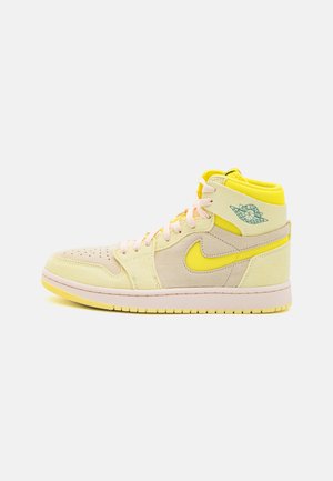 Høj sneaker i beige og gul med lyserøde snørebånd, gul sål og turkis Air Jordan-logo på siden, vist på hvid baggrund.