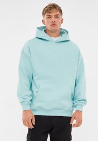 Felpa blu chiaro con una grande tasca frontale, cappuccio regolabile con lacci, polsini a coste e vestibilità comoda. Tessuto liscio senza alcun motivo.