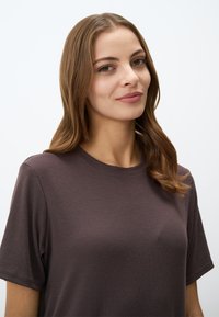 T-shirt marron à côtes avec des manches courtes et un col rond, présentant une texture douce et une coupe décontractée. L'arrière-plan est complètement blanc.