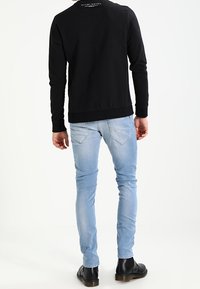 Svart crewneck sweatshirt med ribbad mudd, bärs över ljusblå slim-fit jeans med kontrasterande sömmar och bakfickor, avslutat med svarta stövlar.