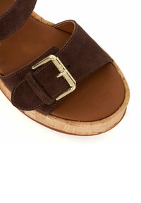 Sandale en suède marron avec une seule sangle et une boucle dorée, un pied en liège et un intérieur lisse marron. Design de semelle arrondie.