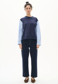 Felpa navy con maniche a righe azzurre, abbinata a pantaloni straight-leg in denim scuro e ballerine con stampa leopardata. Design semplice e moderno.