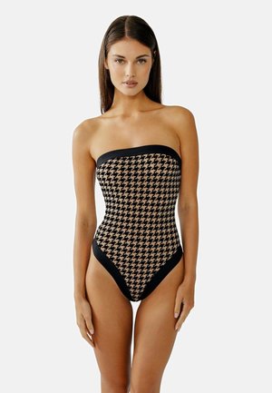 Strapless een-delig zwemkostuum in zwart en beige houndstooth-stijl. Bevat een gladde textuur met stevige zwarte accenten langs de randen.