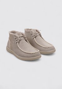 Botas de tobillo de ante beige con un suave forro de piel de invierno, punta redonda, acentos acolchados y suela de goma texturizada. Presentan un cierre de cordones.