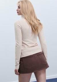 Beige Strickpullover mit langen Ärmeln, kombiniert mit einem braunen Jeansrock. Der Pullover hat einen gerippten Saum und der Rock verfügt über Gesäßtaschen.
