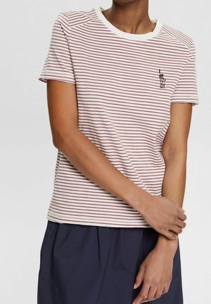 Personne portant une chemise à manches courtes blanche rayée de rouge clair avec une petite broderie noire de la Statue de la Liberté sur la poitrine.