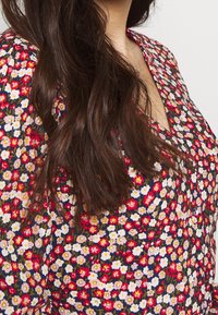 Blusa floreale con uno sfondo blu navy e fiori rossi, rosa e bianchi. Tessuto leggero con scollatura a V e dettagli di cucitura delicati.