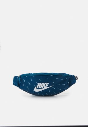 Sac banane Nike bleu avec plusieurs petits logos swoosh blancs et un grand logo Nike blanc à l'avant, avec un compartiment principal zippé.