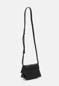 Černá texturovaná kožená kabelka přes rameno s nastavitelným tenkým popruhem a klopovým zapínáním, zobrazena na bílém pozadí.