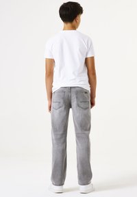 Jeans de mezclilla grises con un corte relajado, cinco bolsillos y detalles de costura sutiles, acompañados de una camiseta blanca simple y zapatillas blancas.
