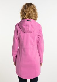 Rosa huva kappa med figursydd midja, mjukt tyg och sömdetaljer. Har en drarhuva och en böjd nederkant, bärs med mörka byxor.