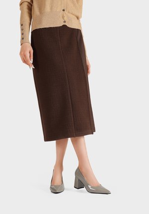 Jupe en laine marron jusqu'au genou avec une finition texturée, assortie à des chaussures à talons carrés en cuir verni gris. Cardigan de couleur beige clair.