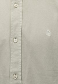 Camisa de botón gris claro, hecha de tela tejida, con una textura suave, botones contrastantes y un pequeño logo bordado en el pecho.