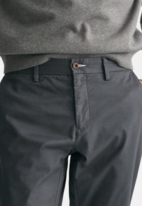 Dunkelgraue, maßgeschneiderte Hose aus glattem Stoff, mit Knopfverschluss und dezenten Steppnähten. Sauberes Design ohne sichtbare Muster.