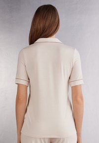 Kortärmad beige polotröja med en mjuk textur, med en klassisk krage och bruna detaljer längs ärmarna och kragen.