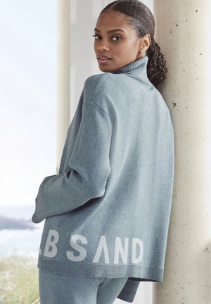 Grauer Strickpullover mit hohem Kragen, in lockerer Passform und mit "SAND"-Textdetail am Saum in hellerem Grau. Glatte Textur.