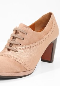 Chaussure beige pour femme en cuir et suède à lacets avec des détails perforés et un talon épais de hauteur moyenne.