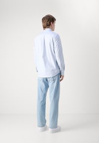 Chemise à manches longues bleu clair avec un pli dans le dos, associée à un jean en denim bleu clair. Coupe décontractée avec des baskets blanches.