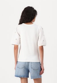 Vit t-shirt med kort ärm och puffärmar, textil med struktur och dekorativa detaljer på ärmarna. Kombinerad med ljusblå denimshorts.