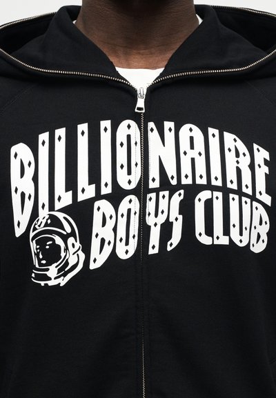 Μαύρο φούτερ με φερμουάρ, με λευκό κείμενο "Billionaire Boys Club" και γραφικό κράνους αστροναύτη στο στήθος, φορεμένο πάνω από λευκό πουκάμισο.