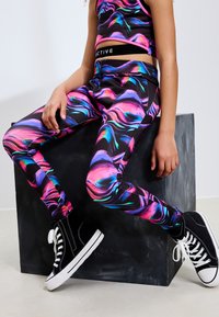 Leggings atletici neri con motivi marmorizzati vivaci in rosa, viola e blu; abbinati a un top corto coordinato e sneakers alte nere.