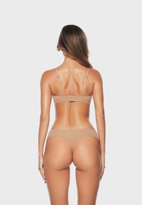 Beżowy zestaw bielizny z bezszwowym biustonoszem i stringami, regulowanymi ramiączkami, miękkim materiałem oraz minimalistycznym designem na białym tle.